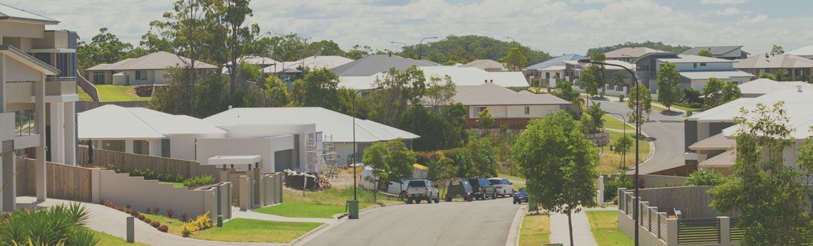 Suburban street with houses and trees under a cloudy sky.