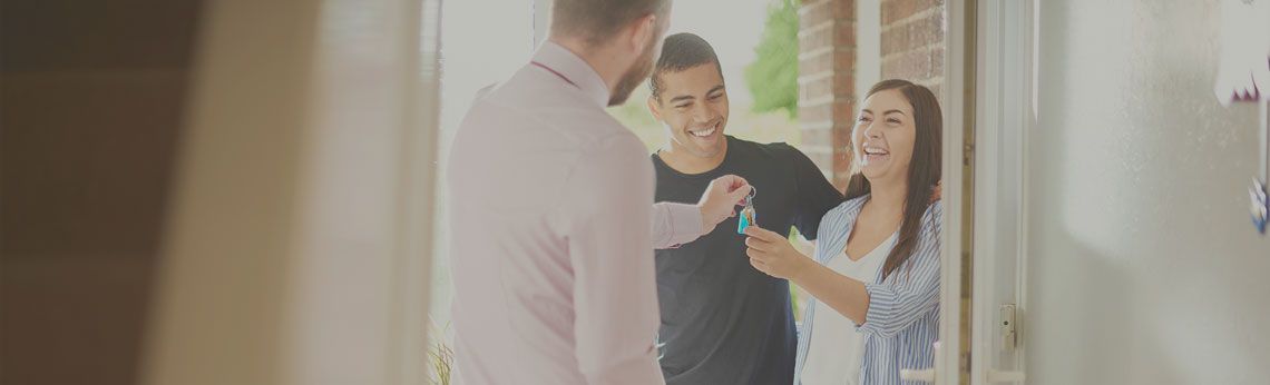 A person hands keys to a couple standing in a doorway.