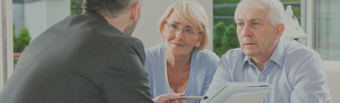 A financial advisor in a suit discusses with a senior couple in a bright office.