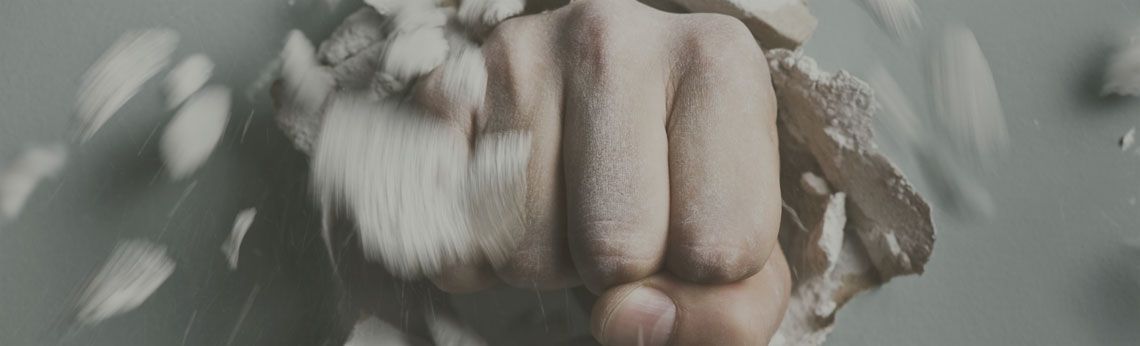 A fist punches through a light-colored surface, causing it to break apart with pieces flying out.