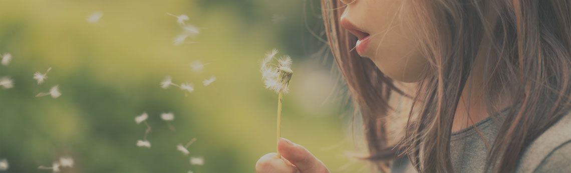 A person blowing on a dandelion, sending seeds into the air. Green background.