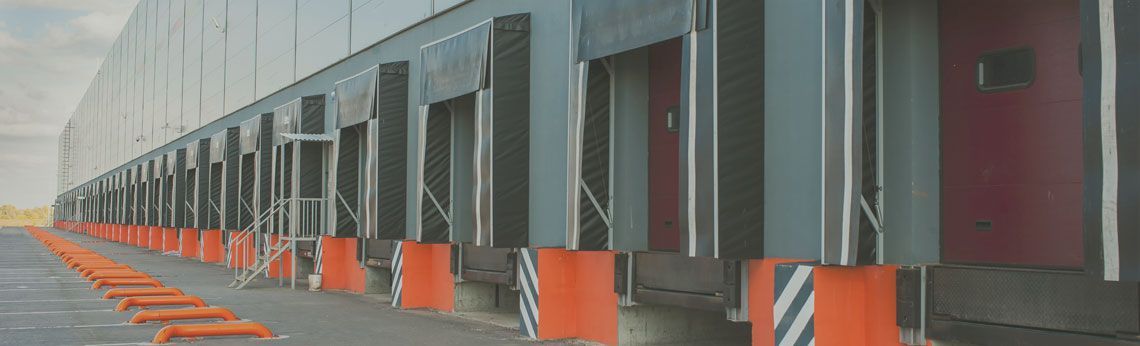 Loading docks of a large industrial building, with orange and black bollards in front.