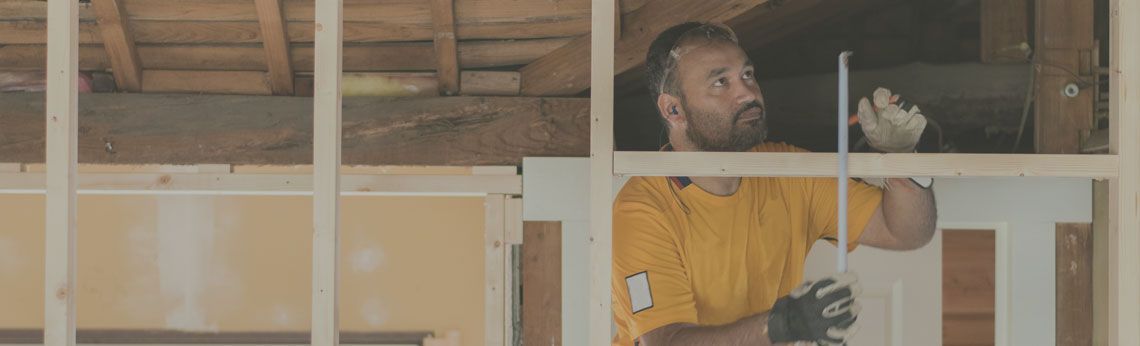 Man in a yellow shirt measuring wood in a construction setting.