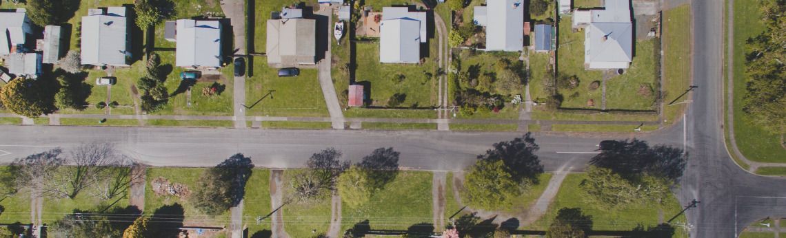Overhead view of houses, a road with trees, and grass in a residential neighborhood.