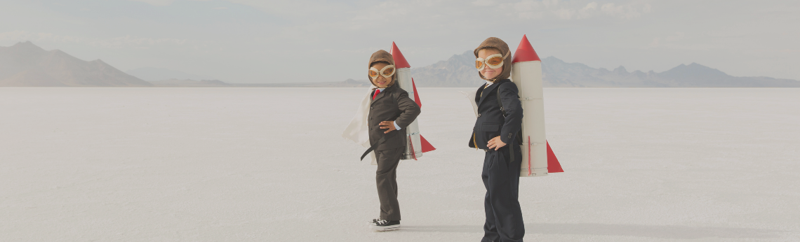 Two people standing on a white expanse, both wearing rocket packs. Mountains in the background.