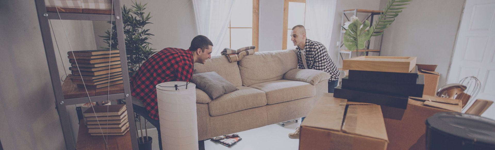 Two people move a sofa in a living room filled with boxes and furniture.