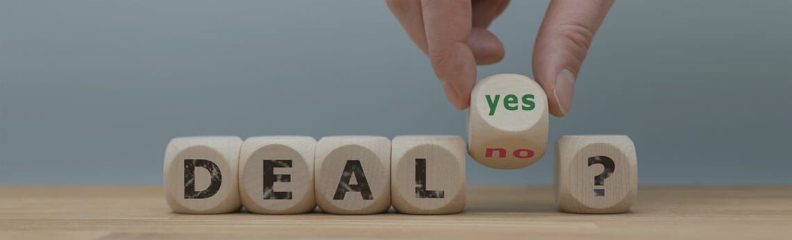 Hand holding a die with “yes” to complete the word “DEAL?” on wooden blocks.