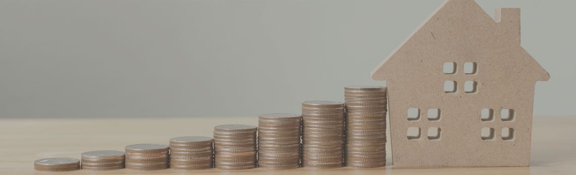 A wooden house next to stacks of coins, representing financial growth.