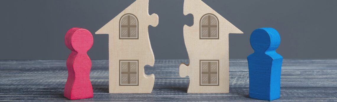 Two wooden figures, one pink and one blue, stand on either side of a split house puzzle.