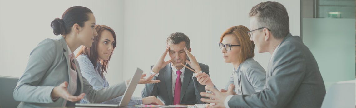 Five people in a business meeting, with one man looking stressed and holding his head.