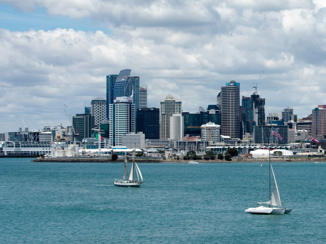 City skyline on waterfront, two sailboats on the water, cloudy blue sky.