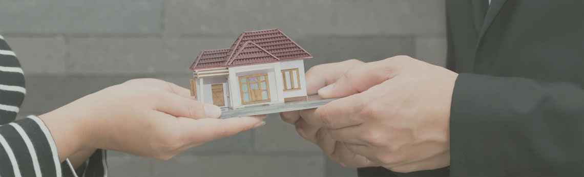 Hands passing a small house model, likely a real estate transaction.
