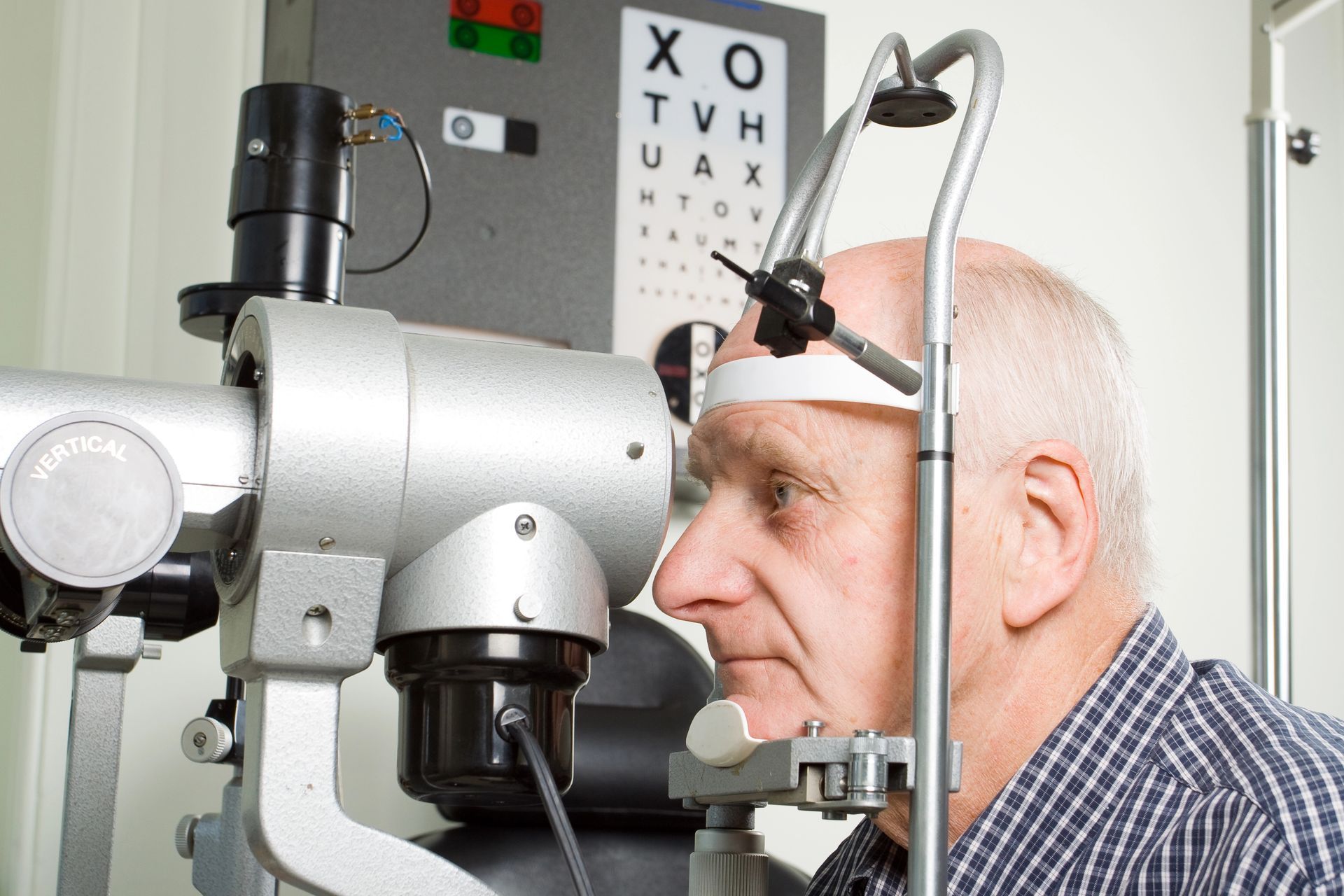 In un ambiente clinico, una persona viene sottoposta a un esame oculistico con lampada a fessura, con una tabella optometrica sullo sfondo.