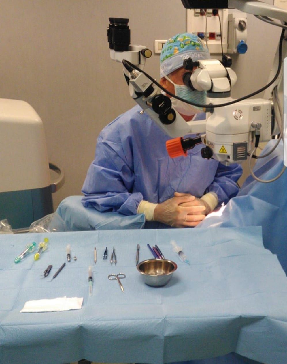 Un chirurgo esegue un intervento di chirurgia oftalmica con l'ausilio di un microscopio, con gli strumenti chirurgici disposti su un vassoio blu sterile.