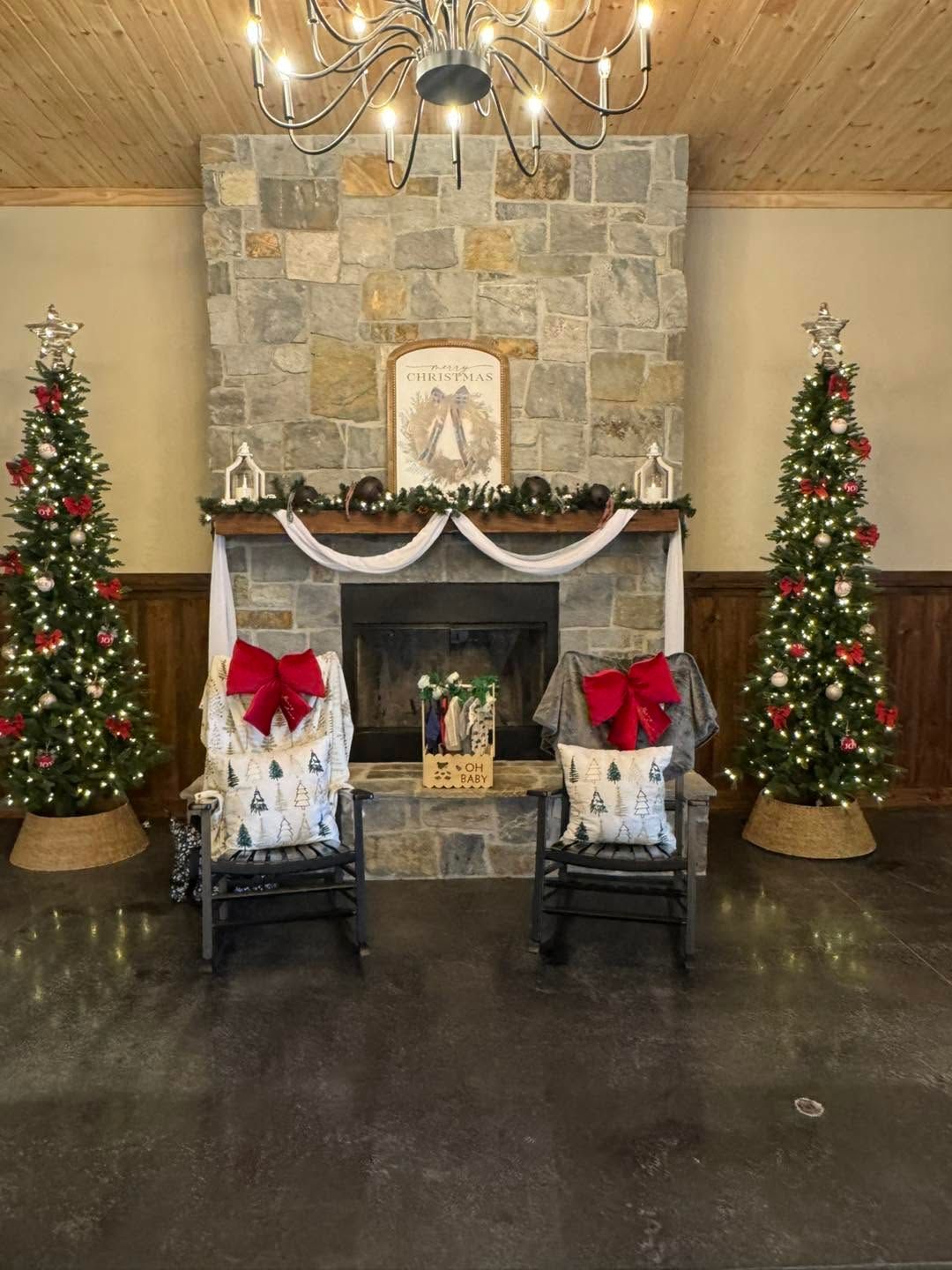 Festive living room with stone fireplace, two Christmas trees, and red-bowed chairs by the hearth