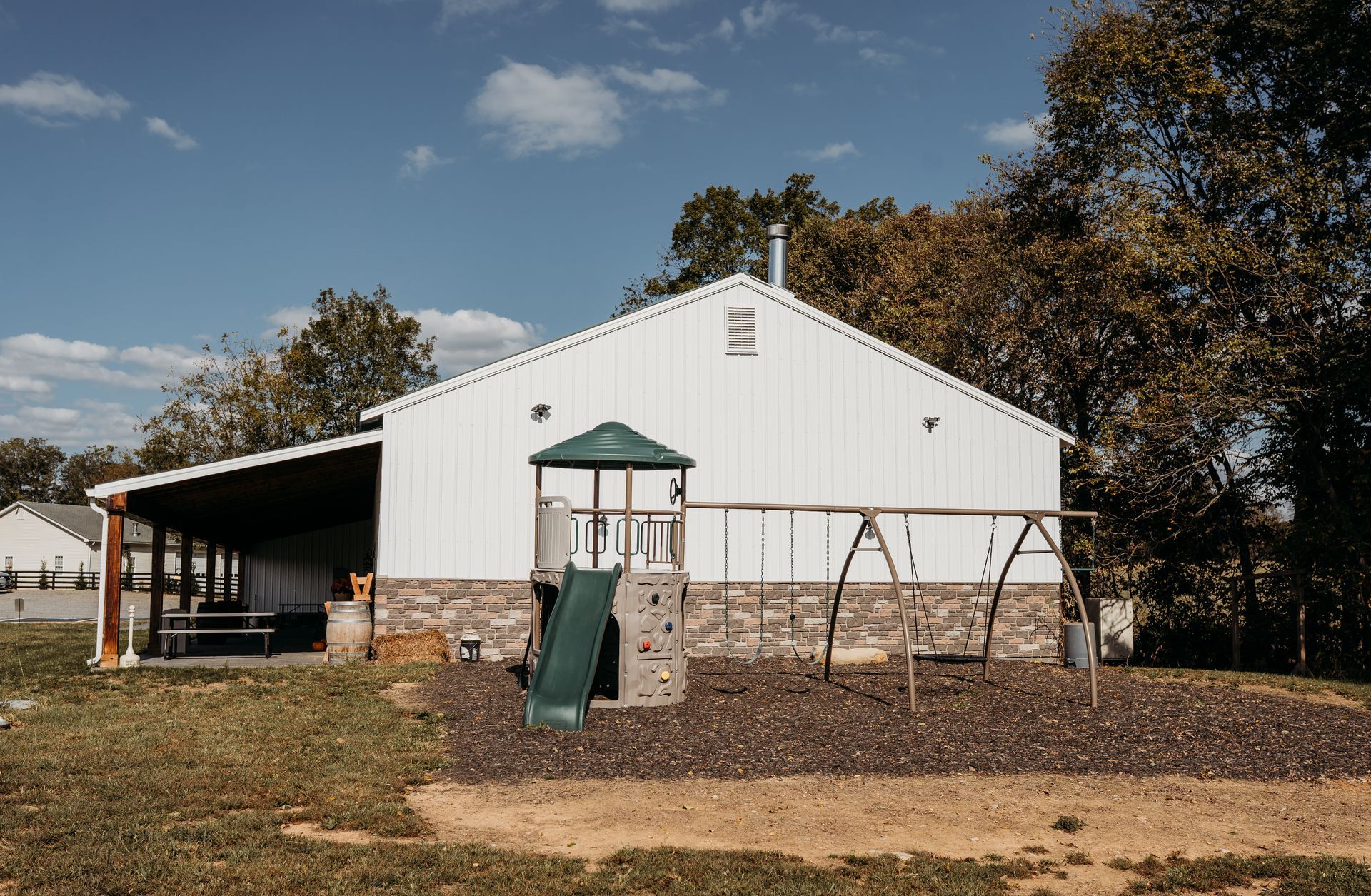 White barn-style building with covered porch and playground swings under a blue sky