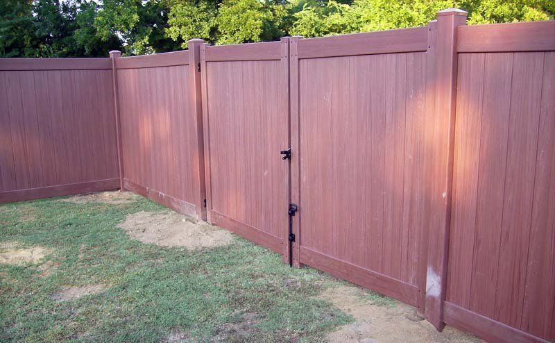 Brown wooden fence with a gate in a grassy yard.