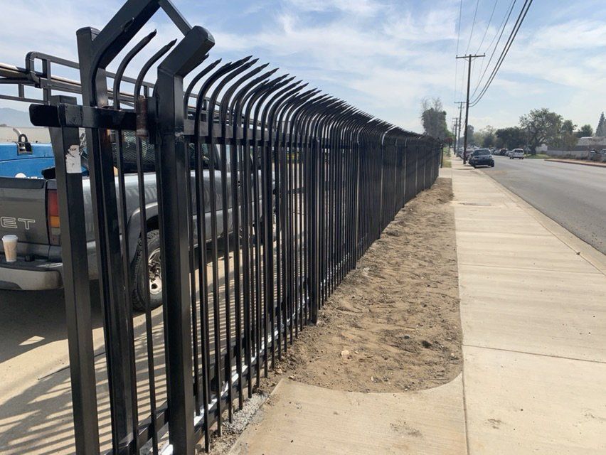 Black metal fence with curved tops along a sidewalk and street.
