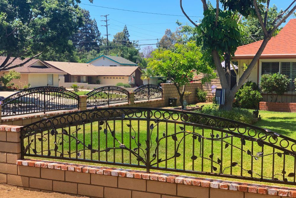 Black metal fence with leaf design atop a brick wall in a residential neighborhood.