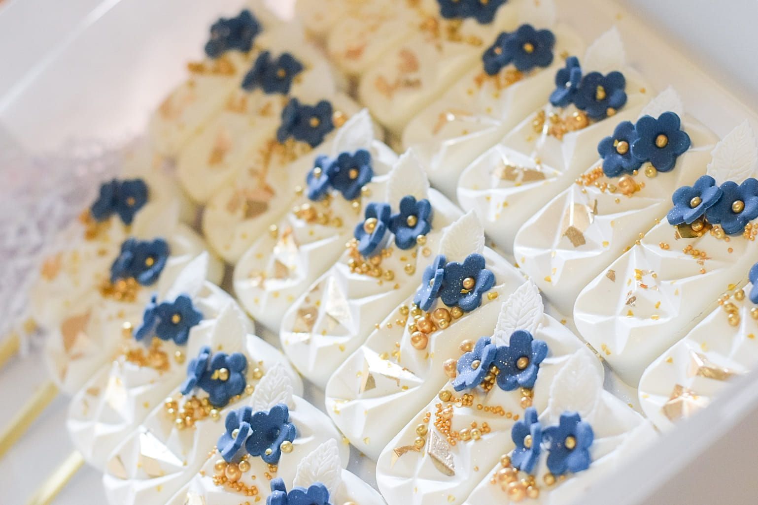 White and gold cookies with blue flower decorations, arranged in a box.