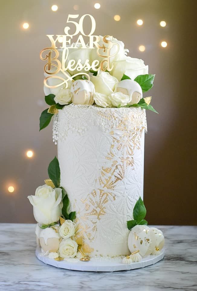 White tiered cake with gold accents, topped with white roses and a 
