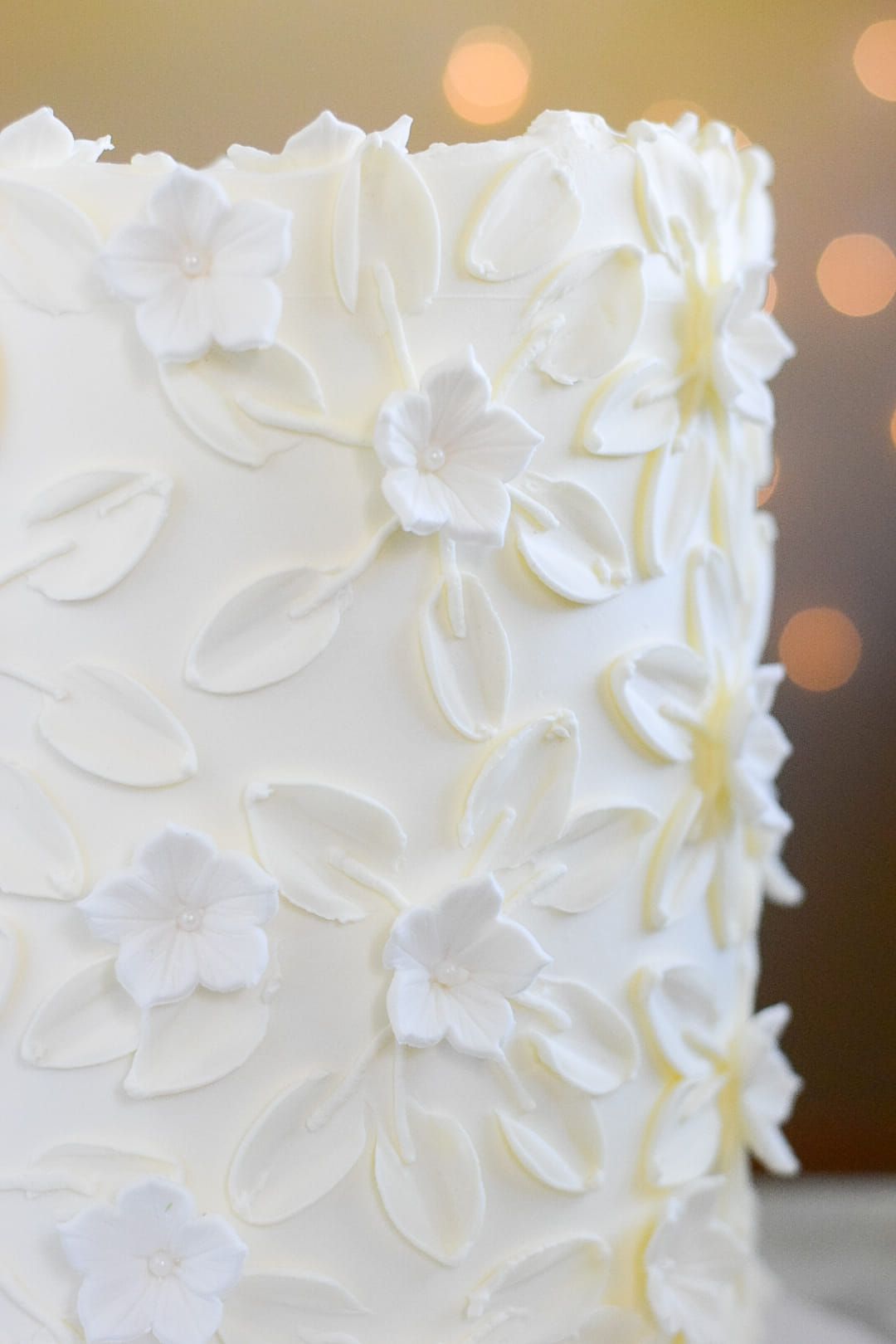 White cake with floral buttercream decorations against a blurred background.