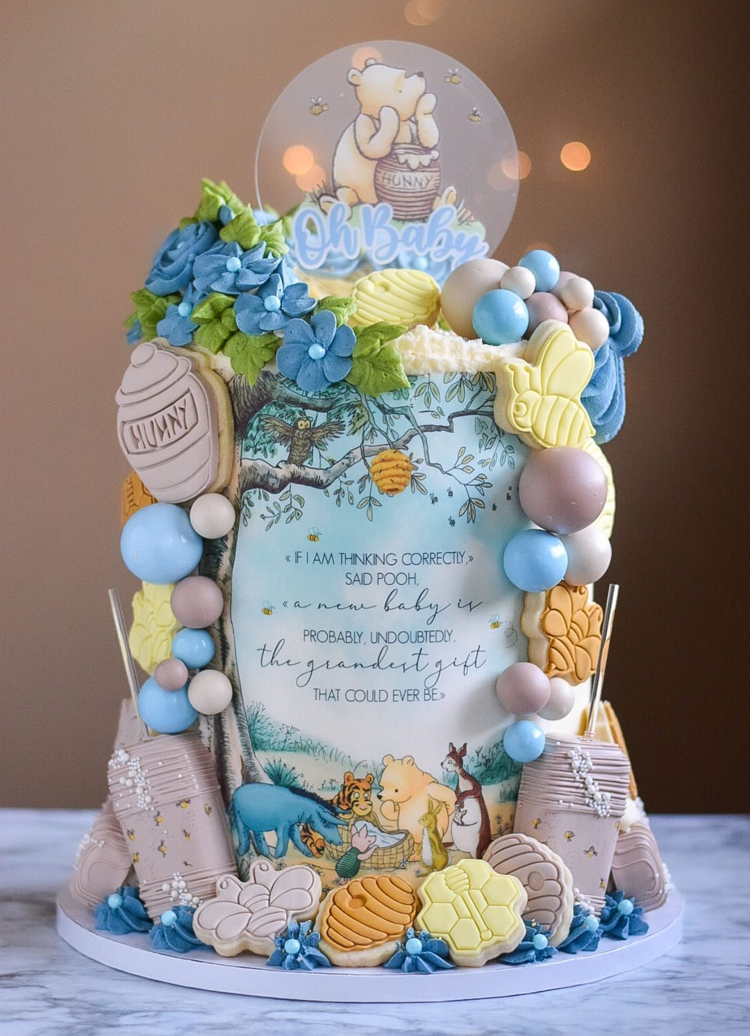 A whimsical Winnie the Pooh baby shower cake, featuring blue and yellow flowers, cookies, and a Pooh topper.