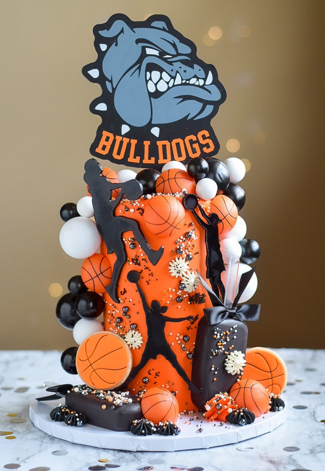 Basketball-themed cake with Bulldogs logo, basketballs, and silhouettes in orange, black, and white.
