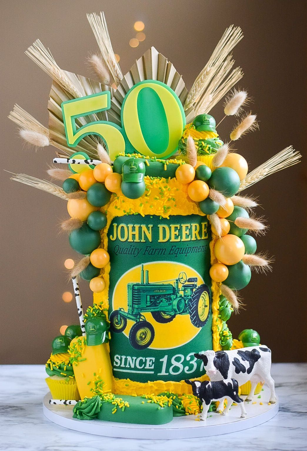 John Deere-themed 50th birthday cake: green and yellow with tractor illustration, balloons, cow, wheat.