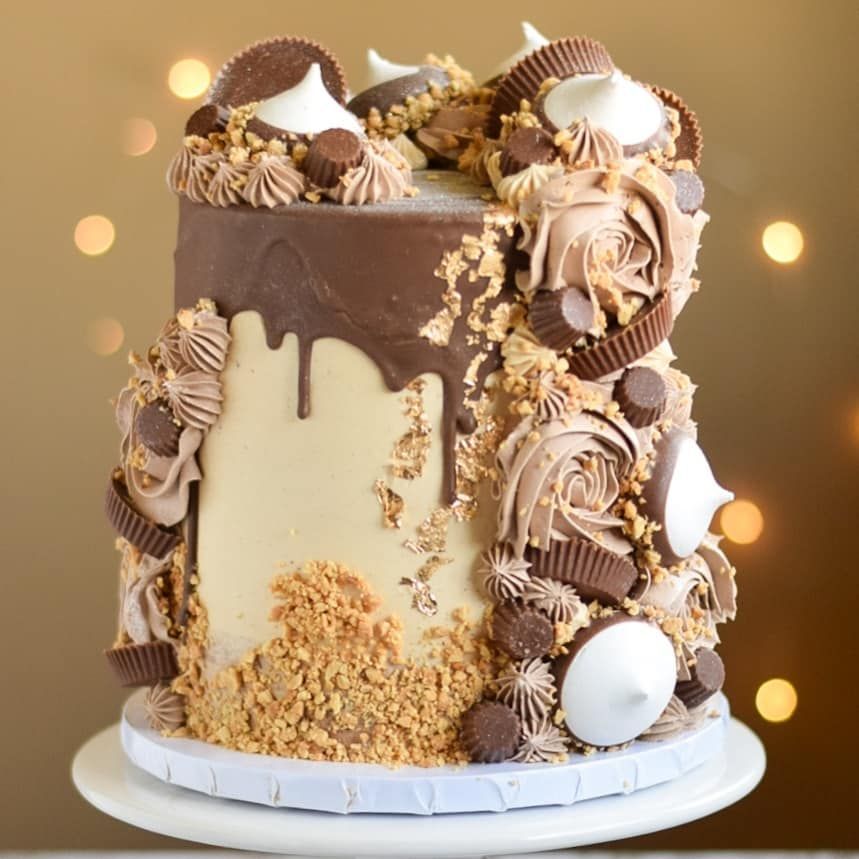 Chocolate cake with peanut butter cups, frosting rosettes, and drips.