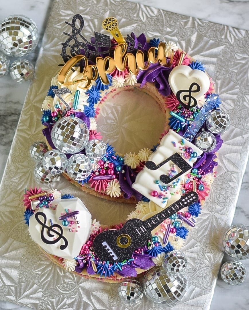 Number nine shaped cake decorated with music themed items, disco balls, and frosting.