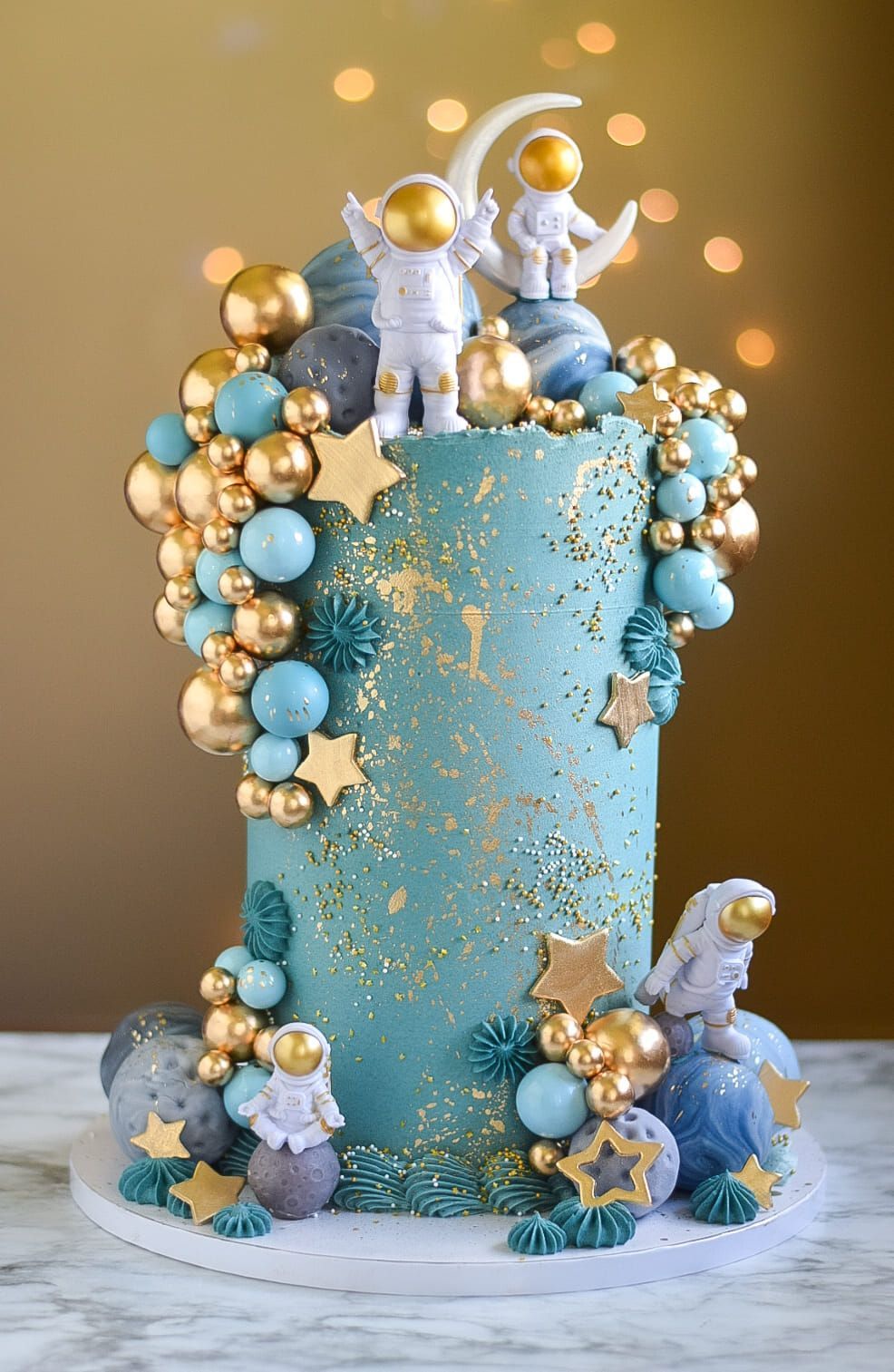 Space-themed cake with teal frosting, golden accents, and astronaut figurines.