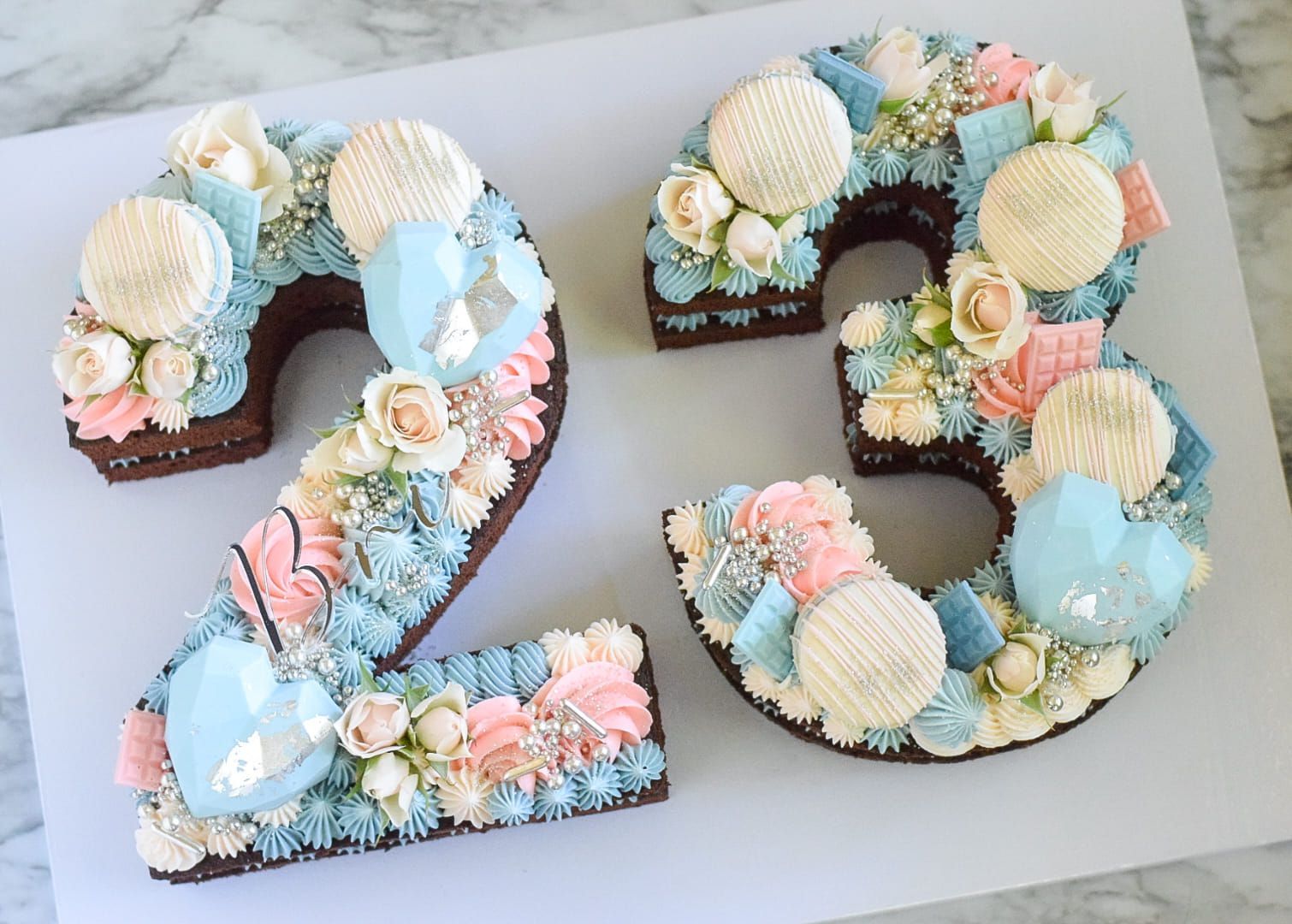 Number-shaped chocolate cake decorated with blue, pink, and white frosting, flowers, and cookies.