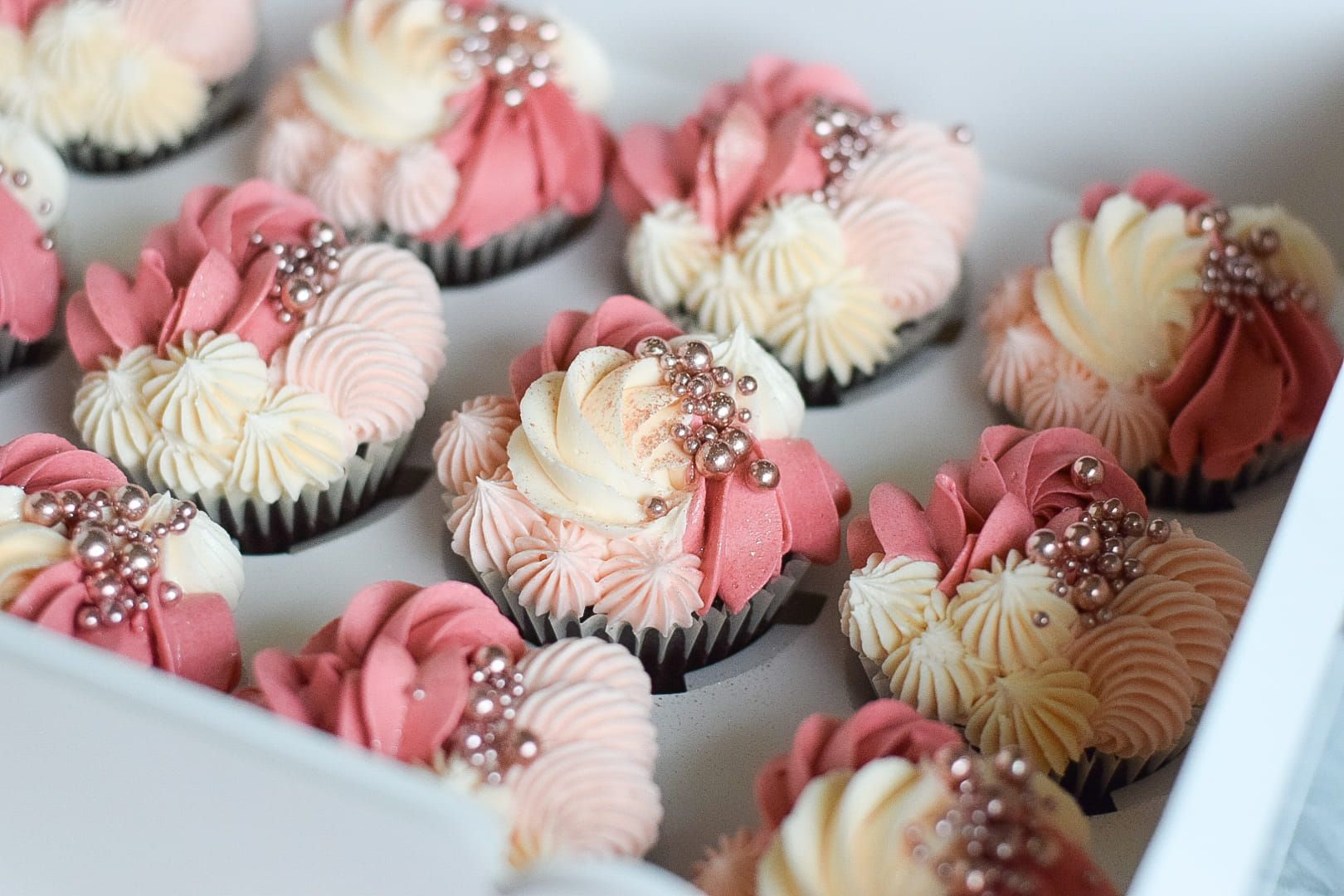 Box of cupcakes with pink and cream frosting, decorated with silver sprinkles.
