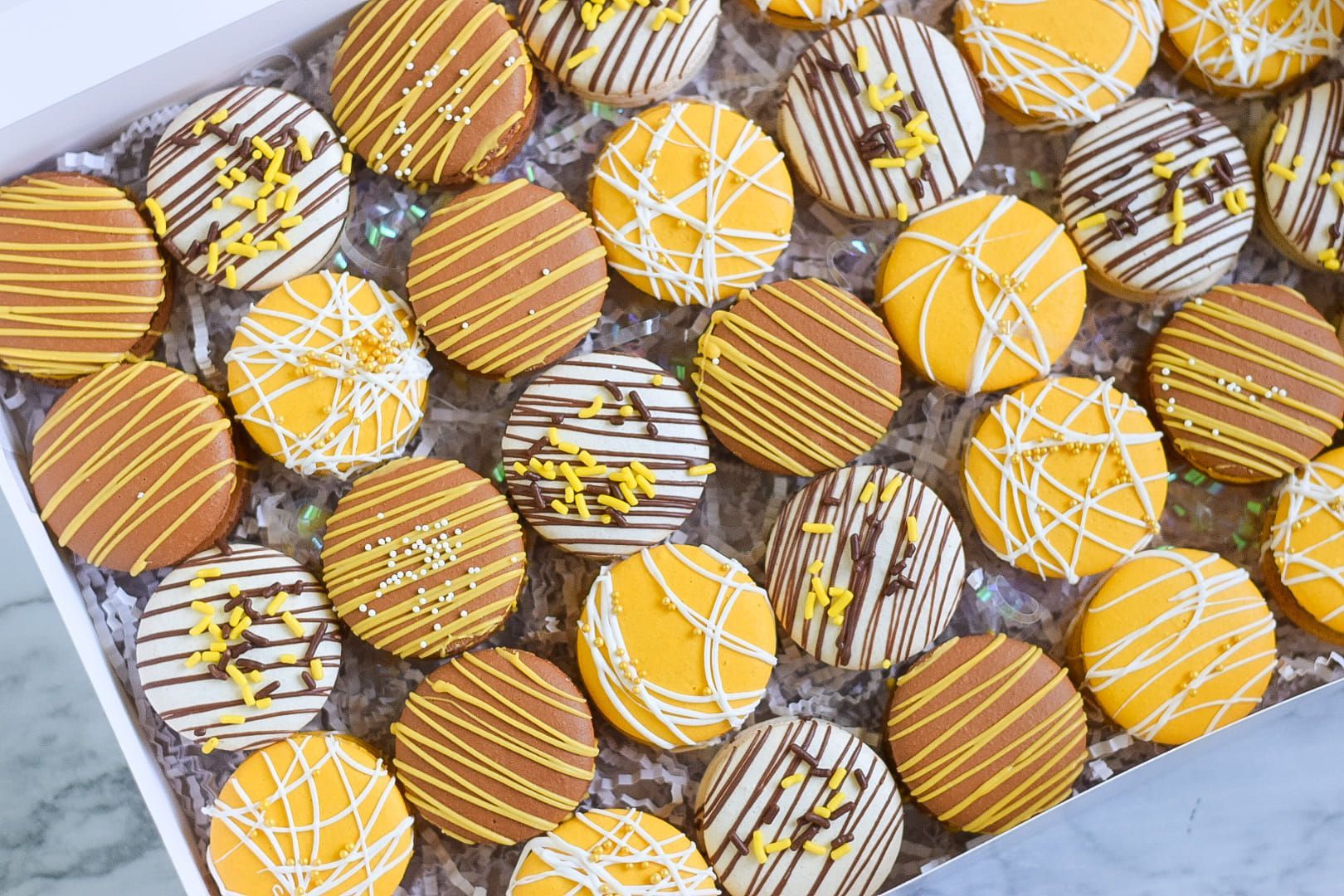 Box of colorful, round, frosted cookies, decorated with drizzle and sprinkles.