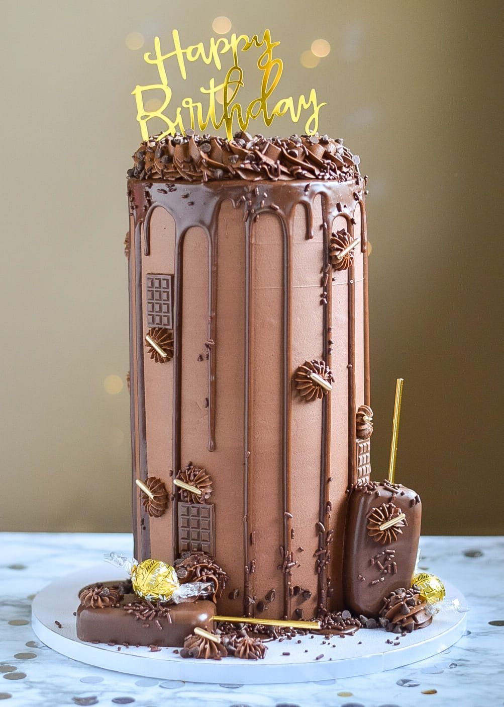 Chocolate birthday cake with drips, decorations, and a gold 
