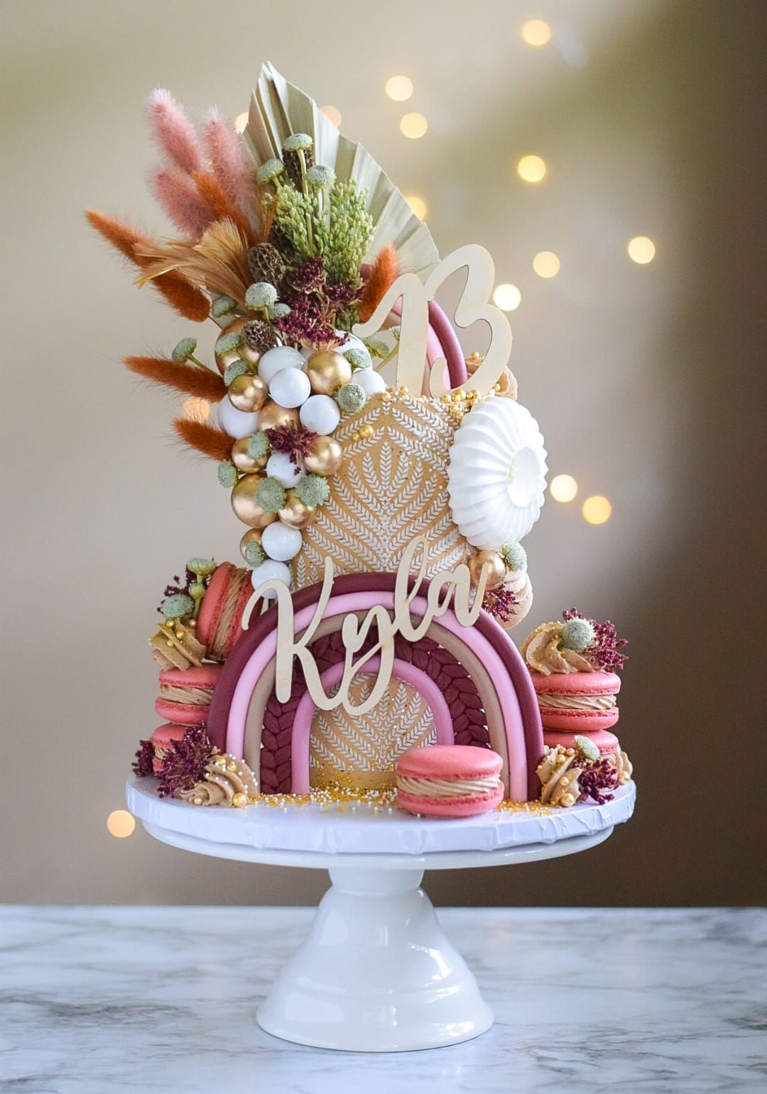 Boho-themed birthday cake with gold accents, macarons, and a rainbow.