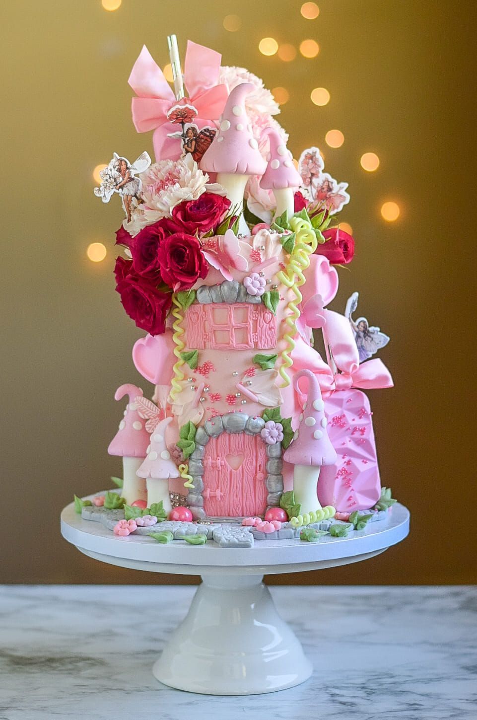 Pink fairytale castle cake with mushrooms, flowers, and decorations on a white pedestal.