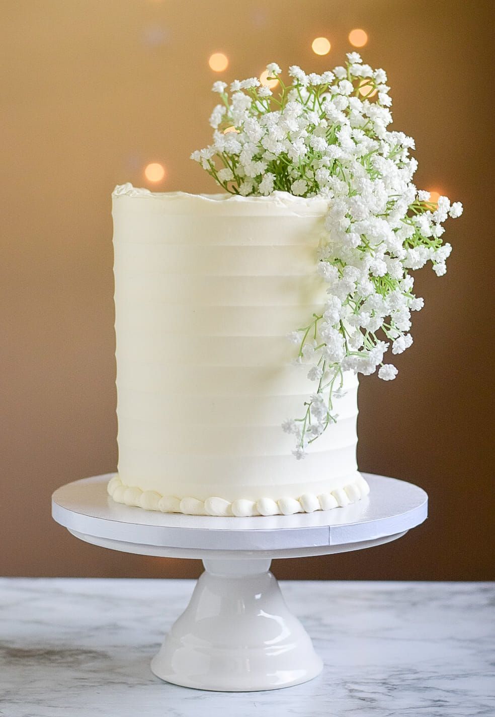 White frosted cake with baby's breath floral arrangement on a white cake stand.