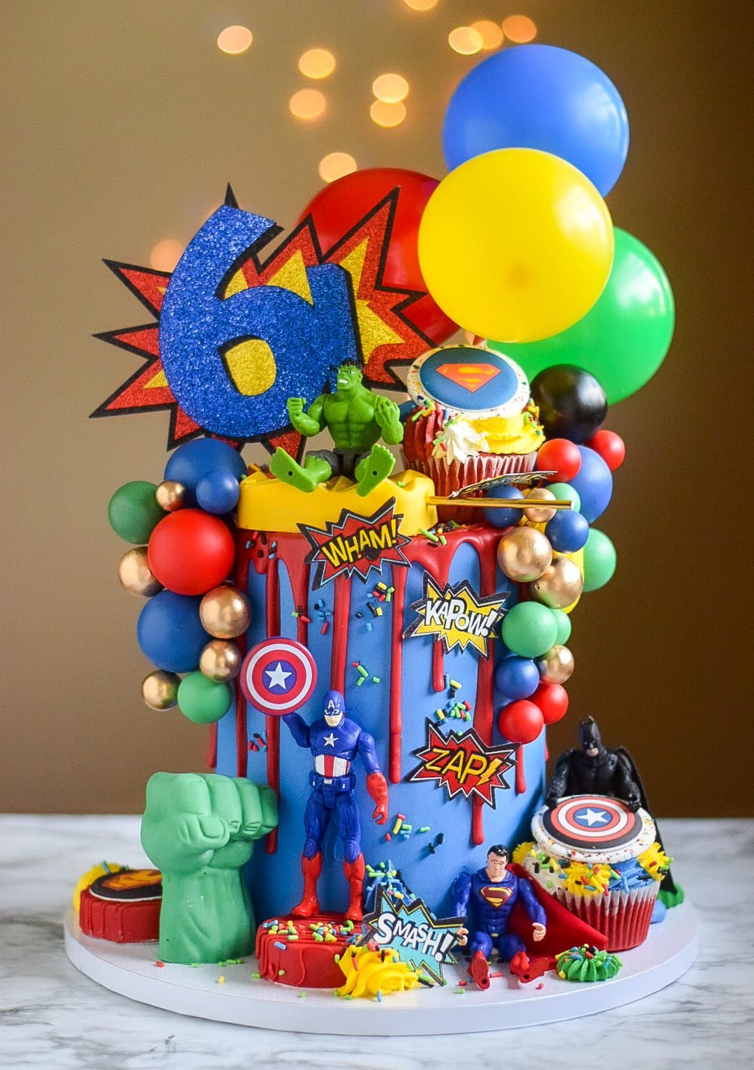 Superhero-themed birthday cake with figures, balloons, and 
