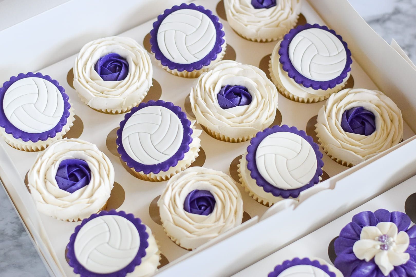 Box of cupcakes: volleyball-themed with purple and white frosting decorations.