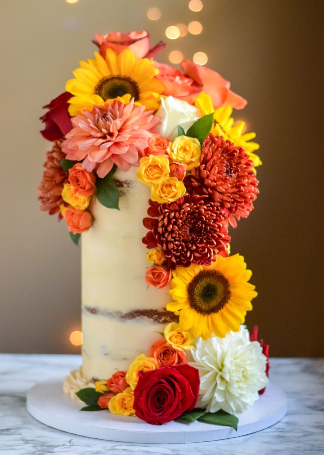 Cake decorated with vibrant sunflowers, roses, and chrysanthemums cascading down the side.