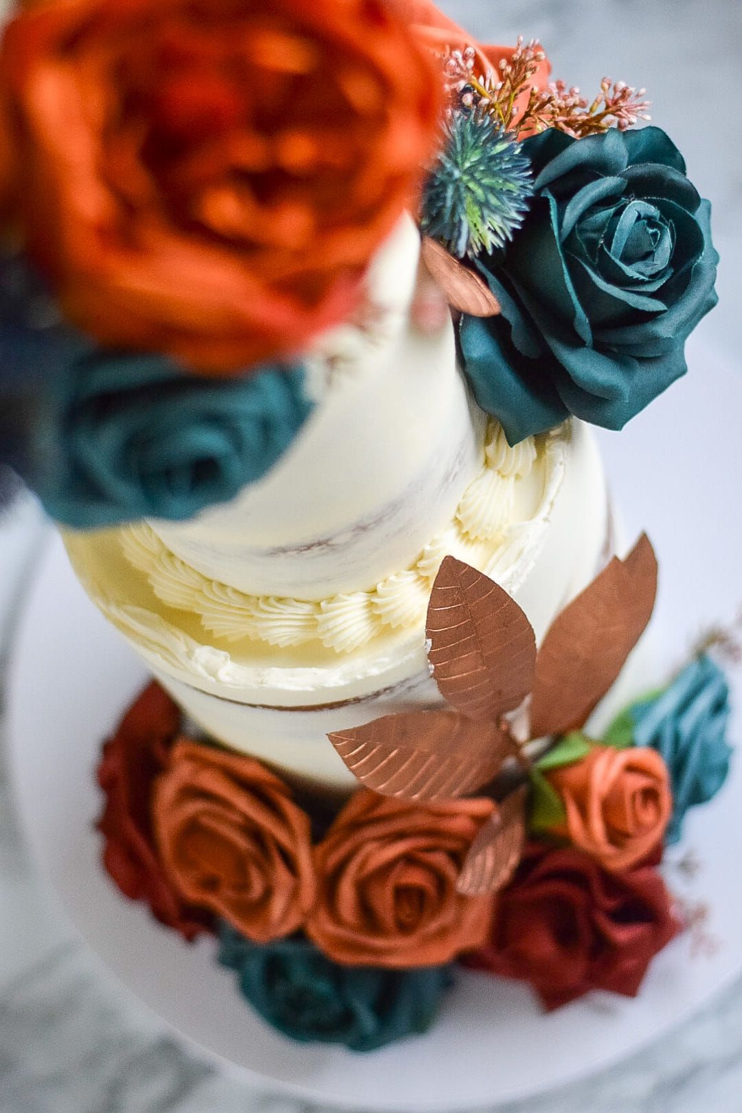 Three-tiered cake with teal and rust-colored floral decorations.