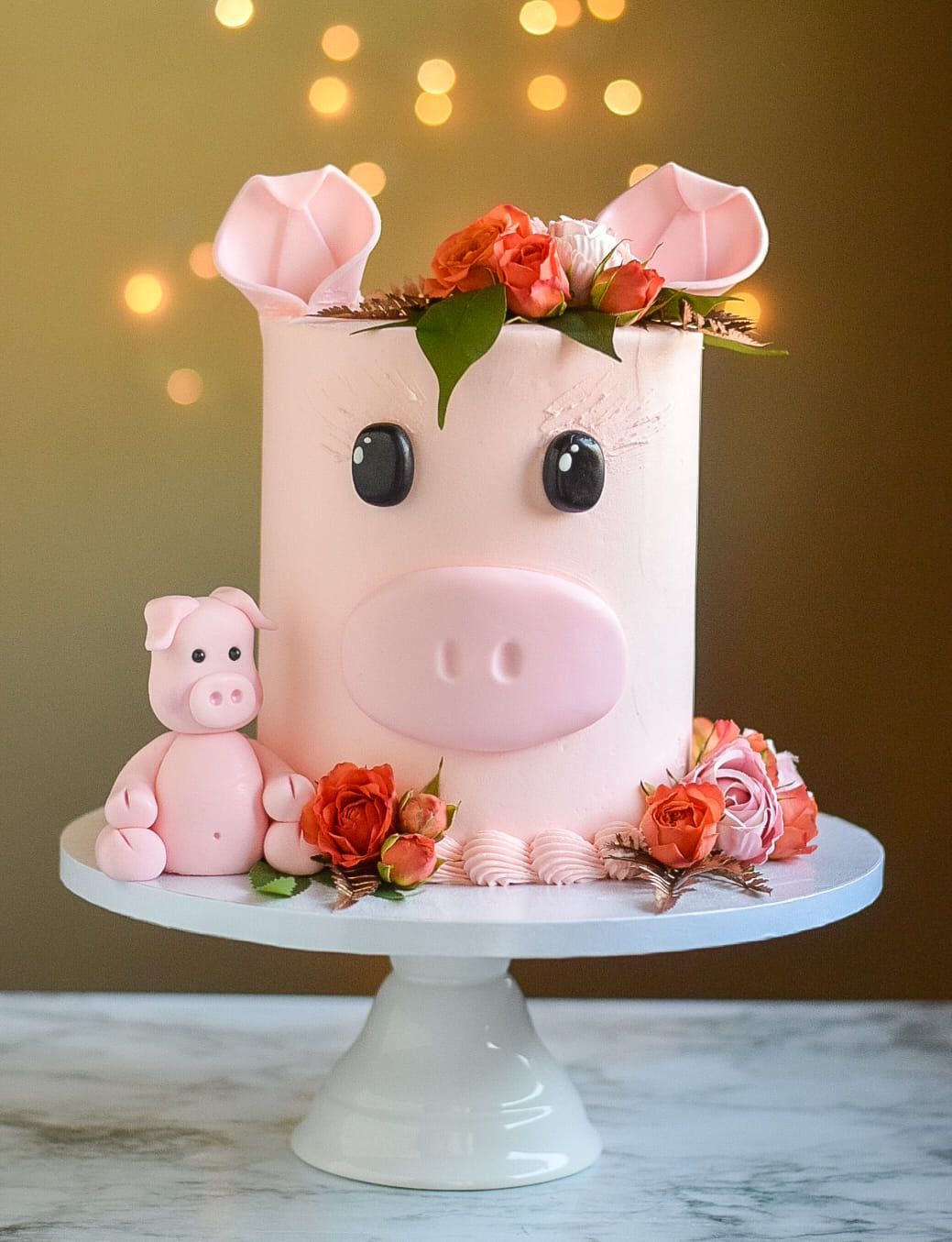 Pink pig cake decorated with flowers and a small pig figurine on a white cake stand.