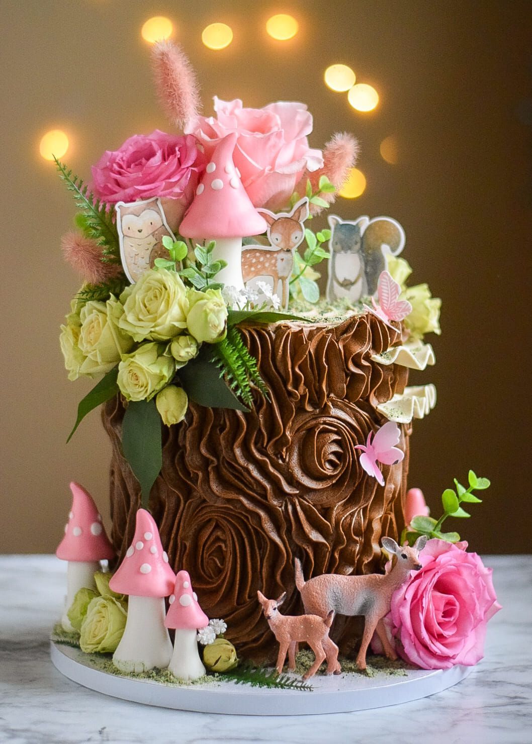 Cake decorated as a tree stump with pink mushrooms, flowers, and woodland creatures.
