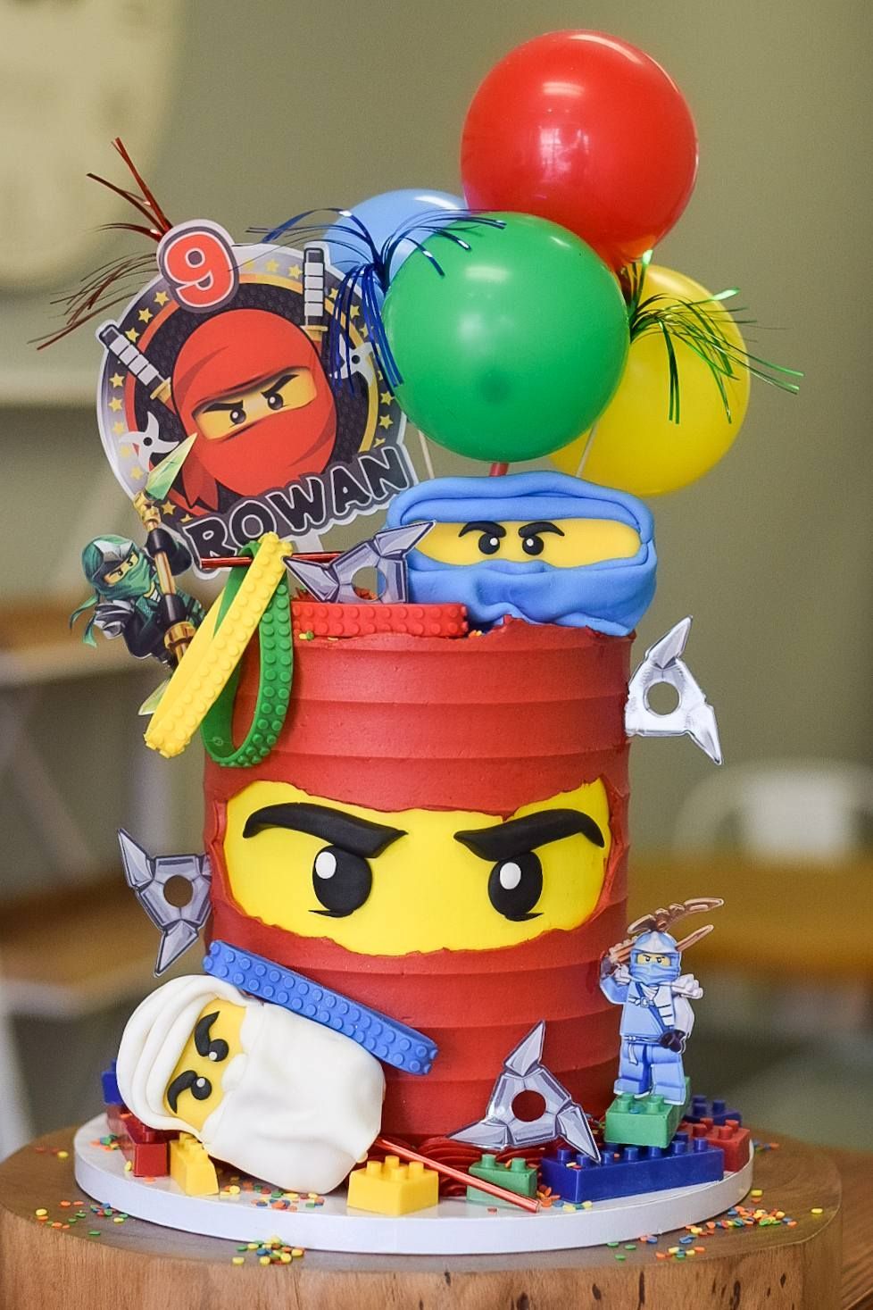 Ninjago-themed birthday cake with red, yellow, and blue fondant, balloons, and LEGO figures.