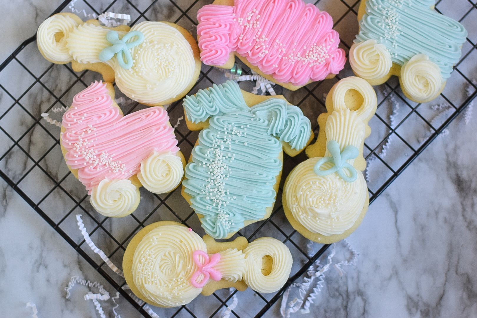Baby shower cookies: stroller, baby clothes, and rattle shaped, decorated with pastel frosting.