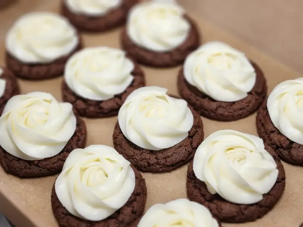 Chocolate cookies topped with white frosting rosettes in a cardboard box.