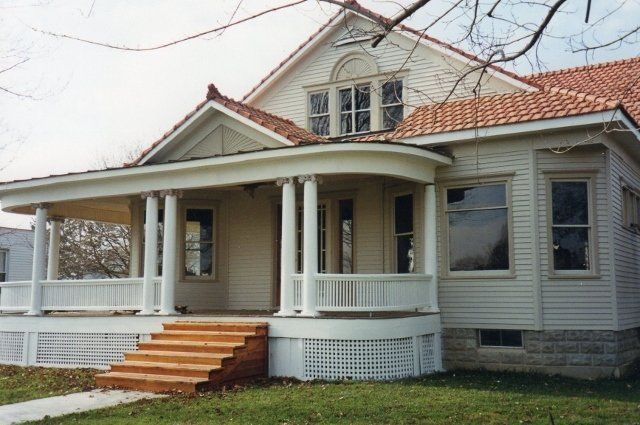 White farmhouse with red-tiled roof, front porch, and steps on a grassy yard
