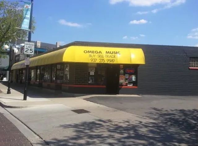 Corner storefront with a yellow awning and glass windows on a sunny street corner.